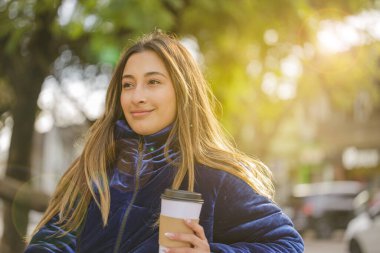 Kahve içen Latin bir kız halka açık bir parkta fotokopi alanı olan bir bankta oturuyor..