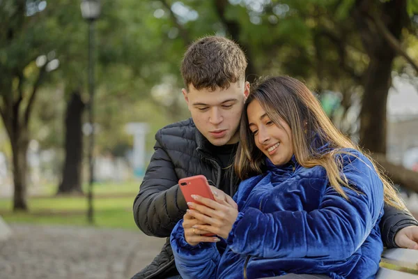 Młoda Para Patrząca Telefon Komórkowy Siedzący Ławce Parku Publicznym — Zdjęcie stockowe