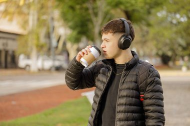 Kulaklıklı bir adam halka açık bir parkta fotokopi çekerken kahve içer..