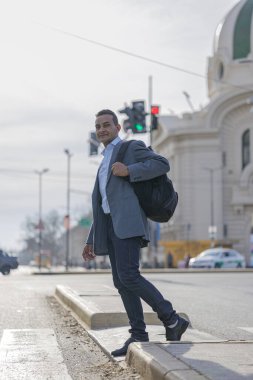 Takım elbiseli ve sırt çantalı Latin bir adam yayanın içinden geçiyor..