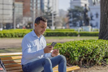 Latin bir adam cep telefonuyla kare bir bankta kredi kartıyla alışveriş yapıyor..
