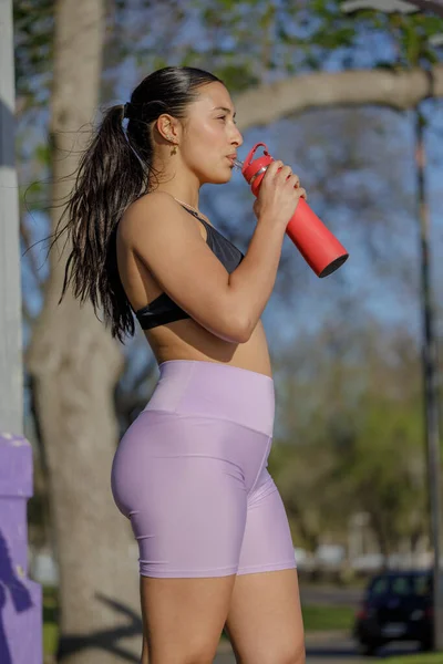 Latin girl in sportswear drinking water.