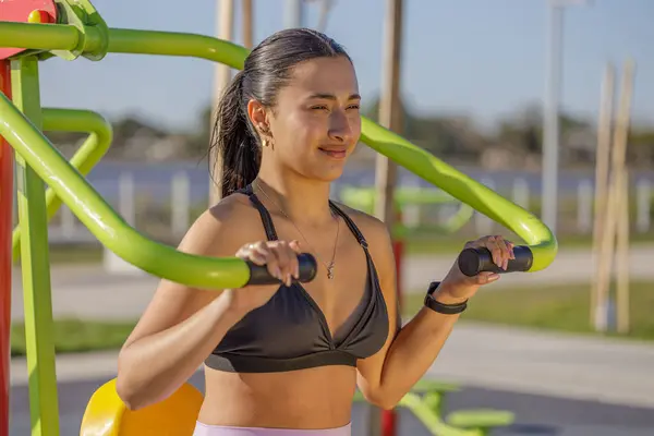 Latin girl exercising her arms on an outdoor exercise machine.