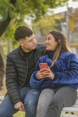 Latin kız ve beyaz çocuk halka açık bir parkta bankta oturuyor..