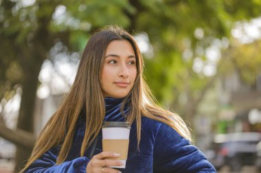 Güzel Latin kız halka açık bir bankta fotokopi alanı olan kahve içiyor..