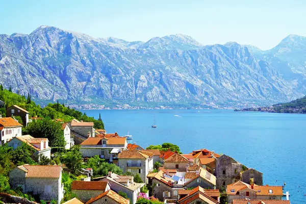 Karadağ 'ın Perast kentinde, parlak deniz ve görkemli dağların zeminine karşı kırmızı kiremitli evler.