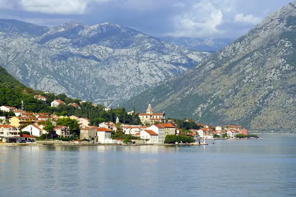 Karadağ 'ın Prcanj kentinde, dağların arka planına karşı Bakire Meryem Kilisesi ile Kotor Körfezi' nin karşı kıyısından manzara