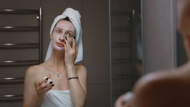 Daily beauty treatment - woman massaging her face before bath mirror