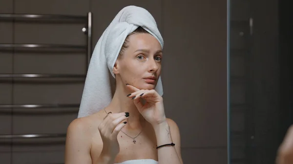 Wanita Dengan Handuk Melilit Kepalanya Memijat Wajahnya Sebelum Cermin Mandi Stok Gambar
