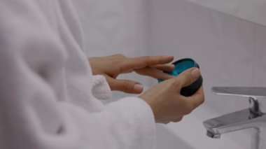 Kafasına havlu sarılmış genç ve çekici bir kadın. Renkli yüz temizleme maskesi takıyor. Günlük sabah rutini - yüz temizleme, cilt bakımı, kabuk soyma, nemlendirici ve güzellik tedavi konsepti