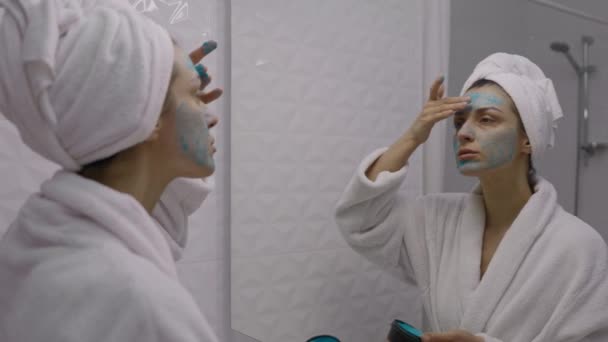 年轻迷人的女人 头上缠着毛巾 涂上彩色洗脸面罩 每天早上的日常事务 面部清洁 润肤及美容美发概念 — 图库视频影像