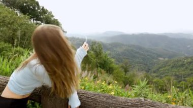 Young tourist woman enjoys the view from a wooden bridge high in the mountain designed for viewing the side from above. in the jungle. Vivid image of the mountain. Tourism destination. High quality 4k