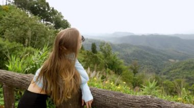 Young tourist woman enjoys the view from a wooden bridge high in the mountain designed for viewing the side from above. in the jungle. Vivid image of the mountain. Tourism destination. High quality 4k