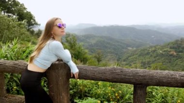 Young tourist woman enjoys the view from a wooden bridge high in the mountain designed for viewing the side from above. in the jungle. Vivid image of the mountain. Tourism destination. High quality 4k