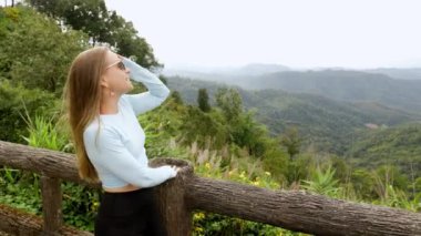 Young tourist woman enjoys the view from a wooden bridge high in the mountain designed for viewing the side from above. in the jungle. Vivid image of the mountain. Tourism destination. High quality 4k