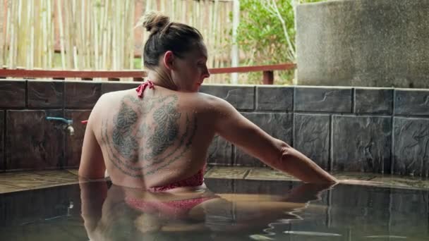 Kobieta Wysportowanym Ciałem Tatuażem Tygrysa Plecach Siedzi Gorącym Basenie Ugniata — Wideo stockowe