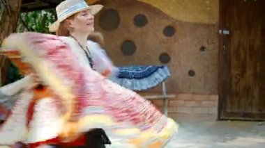 Çok renkli bornozlu bir kadın ormanda, doğadaki bir evin önünde neşeyle dans eder ve diktiği etekleri gösterir. Yüksek kalite 4k görüntü