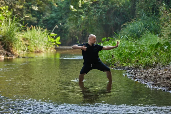Practice makes perfect: A man performing qigong and taijiquan in a jungle river. High quality photo