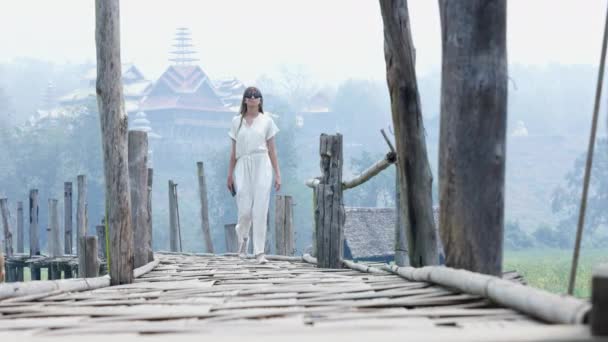 在一个雾蒙蒙的早晨 一个身穿白色衣服的年轻女子在一座木桥上行走 渐渐走近摄像机 高质量的4K镜头 — 图库视频影像