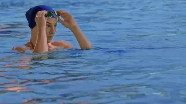 一个戴着护目镜的职业游泳运动员站在游泳池边的前景色 一名女子游泳运动员调整她的眼镜 并开始在镜头前进行训练游泳 慢动作 高质量的4K镜头 — 图库视频影像