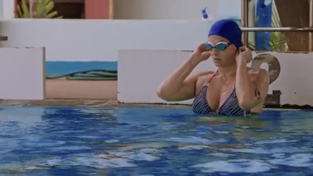 プールでゴーグルでプロの女性スイマーのサイドビュー 女性の水泳者は 水のプールでゴーグルを調整し 泳ぎ始めます クローズアップ スローモーション 高品質の4K映像 — ストック動画