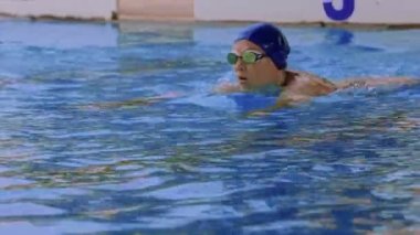Havuzda gözlüklü profesyonel bir kadın yüzücünün yan görüntüsü. Bir kadın yüzücü su havuzuna dalıyor. Yakın çekim, yavaş çekim. Yüksek kalite 4k görüntü