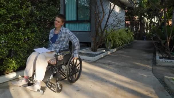 Genç Bir Kadın Kucağında Bir Kitapla Parkta Tekerlekli Sandalyede Yürüyor — Stok video