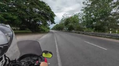 Sessiz bir Tayland otoyolunda 4K 'lık sakin bir motosiklet yolculuğu. Yol işaretleri ve dikiz aynasında sürücüyü gösteren yemyeşil bir arazi. Seyahat ve yaşam tarzı içeriği için ideal bir POV tarafından çekilen.