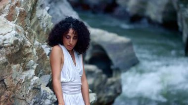 Huzurlu deniz kıyısında derin derin düşüncelere dalan genç bir kadın akıntılı giysiler içinde kayalara hafifçe dokunur. Güzellik ve sükunete daldırılır. Yüksek kalite 4k görüntü