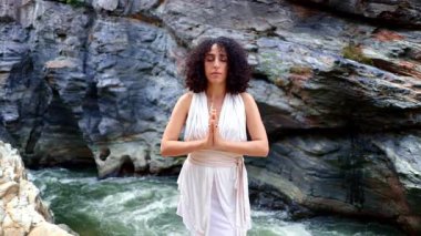 Doğayla Huzurlu Bir Bağlantı: Akan Beyaz Giysili Bir Kadın, Görkemli Kaya oluşumlarıyla çevrili bir Şelale ile Meditasyon Yapıyor. Yüksek kalite 4k görüntü