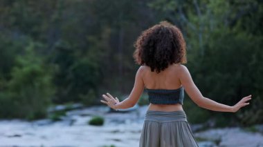 Kıvırcık Saçlı Genç Bir Kadın Nehir Kıyısı 'ndan Huzur Buldu, Altın Saat Döneminde Rüya Gibi Bir Saatteki Doğa Güzelliğini Kucakladı. Yüksek kalite 4k görüntü