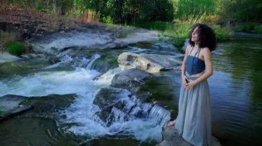 Nehir kıyısında sakin bir an: Bir Kadın, Süzülen Su ve Berrak Yeşillik Ortasında Dururken Doğayı ve İç Huzuru Kucaklar. Yüksek kalite 4k görüntü