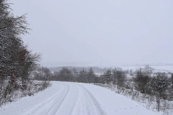 Scenic view of empty, not cleared road with snowy landscape during snowfall in winter season. Right turn onto a slippery winter road. A gloomy winter day. Ukraine.