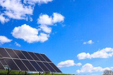 Açık havada çalışan bir güneş pili tesisi. Doymuş mavi bulutlu gökyüzünün arka planında fotoelektrik piller var. Güneş panelleri. Ekoloji, alternatif enerji kavramı
