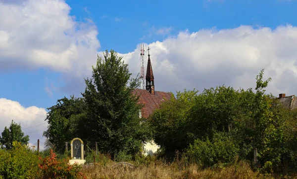 背の高いゴシック様式のカトリック教会のスパイアは 雲で青い空に向かって通信塔と組み合わされました 宗教とカトリック 周りに木や緑がある — ストック写真