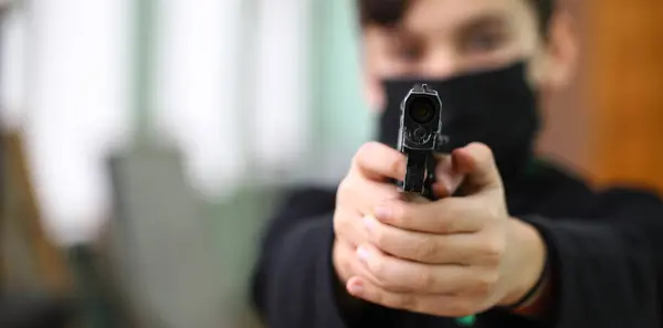 Siyahlı kapüşonlu bir genç silah doğrultuyor. Genç bir adamla silahlı saldırı ve suç kavramı. Silahlı soygun siyah, sığ alan derinliği, silah namlusuna odaklan..