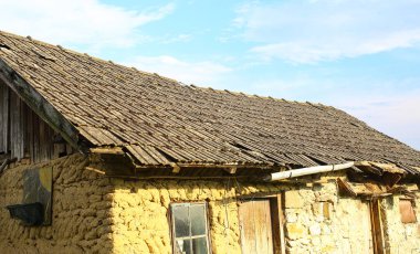 Batan güneşin ışınlarıyla kiremitlerle kaplı eski bir kil bina. Eskimiş malzemeler ve doku. Batı Ukrayna 'nın kırsal bölgesi.