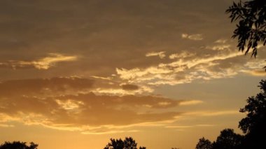 Gökyüzünde bulutlu bulutların yüzdüğü güzel altın bir gün doğumu. Turuncu sabah bulutlu gökyüzü. 4K video