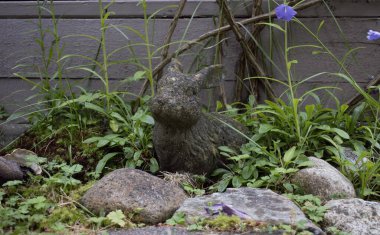 Stone rabbit statue sits in garden framed by bluebells and rocks