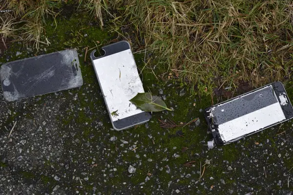 Three broken smartphones on asphalt street