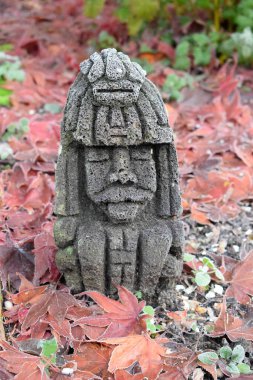 Kırmızı akçaağaç yapraklarının arkasında taş heykel
