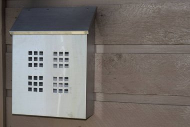Kahverengi ahşap kaplamalı arka planda kare delikleri olan metal posta kutusu