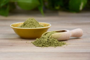 Kratom Mitragyna Specosa tozu tozu görüntüleri. Yeşil kratom ve ahşap kepçe hala hayat dolu fotoğraf. Ahşap arkaplan görüntülerinde Kratom bitkisel ilaçları