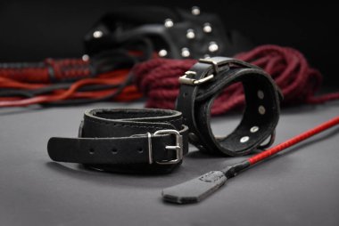 Deri kelepçeler ve kırbaçlanmış fotoğraf görüntüleri. BDSM görüntüleri için seks oyuncakları. Yetişkinler için sadece karanlık arka planda erotik oyuncaklar.