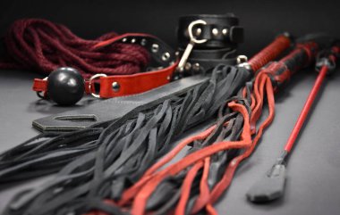 Deri kırbaçlayıcı, arka plandaki fotoğraf çekimlerinde seks oyuncaklarını kamçılıyor. BDSM stok fotoğrafı için erotik oyuncaklar. Yetişkin seks oyuncağı, kırbaç, top susturucusu, kelepçe, ip kenarı görüntüleri.