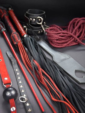 Deri kırbaçlayıcı, arka plandaki fotoğraf çekimlerinde seks oyuncaklarını kamçılıyor. BDSM stok fotoğrafı için erotik oyuncaklar. Yetişkin seks oyuncağı, kırbaç, top susturucu, tasma, ip, kürek, kelepçe resimleri