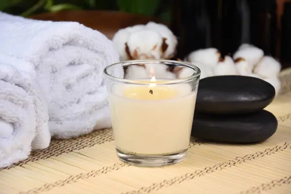 Scented candle, massage stones and white towels spa still life stock photo images. Spa and wellness setting with candle, towels and pebbles on bamboo mat. Beauty spa treatment composition images