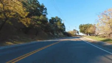 Sakin, ağaçlarla kaplı, açık mavi gökyüzü olan kırsal bir yol güneşli bir günde huzurlu bir sürüş için mükemmel..