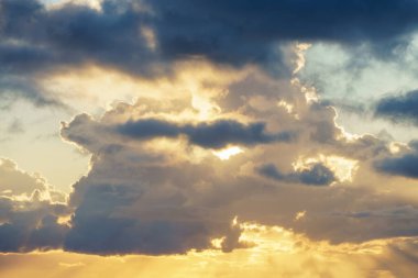 Güneş gün batımında gökyüzündeki bulutların arasından parlıyor, sakin bir atmosferi ve alacakaranlıkta hafif bir rüzgarı olan güzel bir doğal manzara yaratıyor.