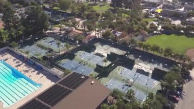 Göz kamaştırıcı bir hava manzarası, pırıl pırıl, canlı bir havuzun yanındaki el değmemiş tenis kortlarını gösteriyor.